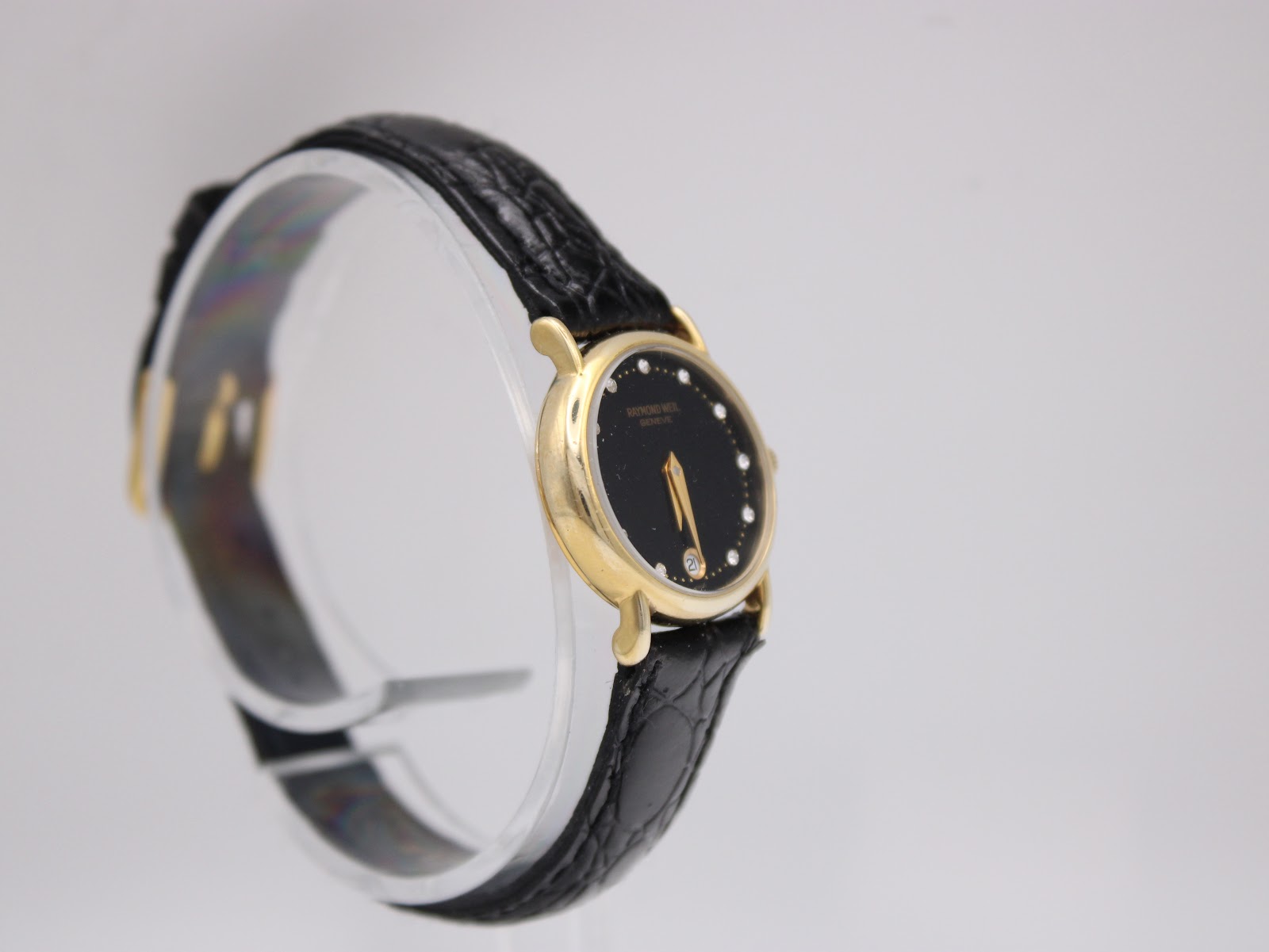Angled side view of the Raymond Weil watch from the left, highlighting the elegant case profile and the crocodile-embossed texture of the black strap.