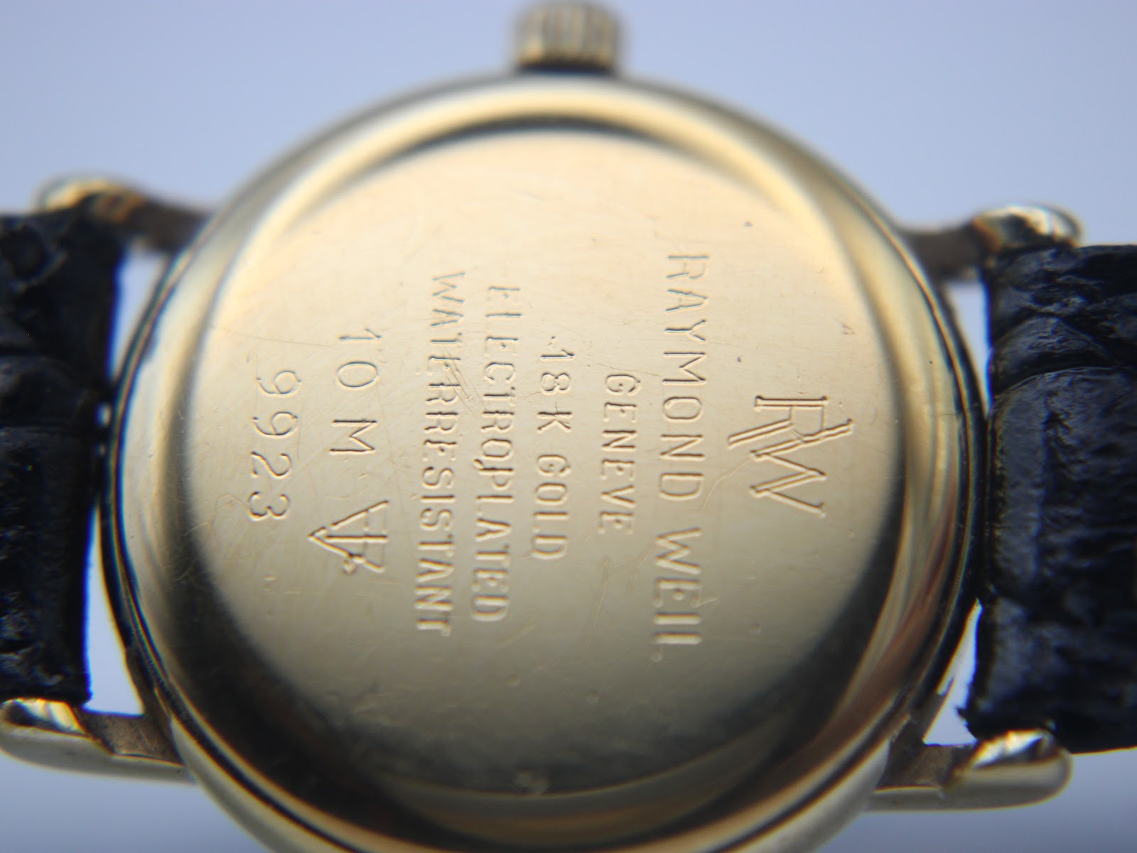 Close-up of the watch's gold-plated case back, clearly engraved with 'RAYMOND WEIL GENEVE', 'RW' logo, '18 K GOLD ELECTROPLATED', 'WATER RESISTANT 10 M', and '9923'.