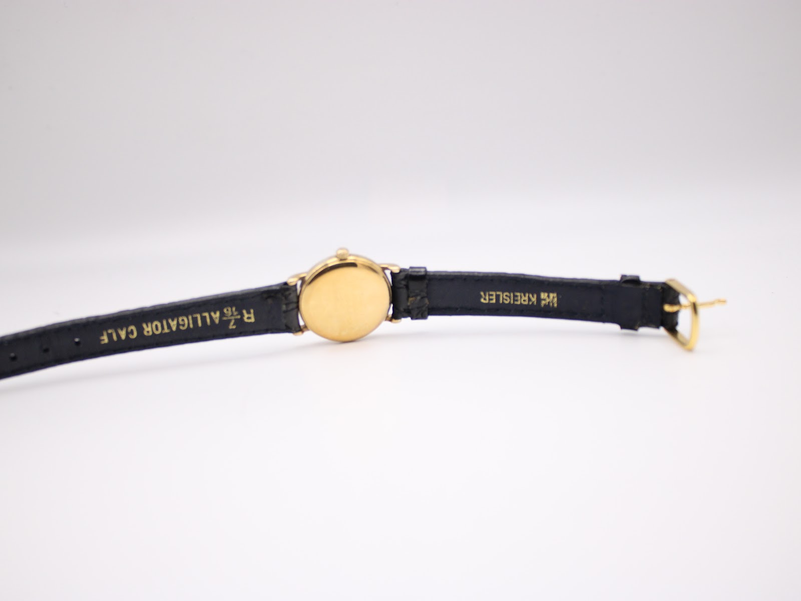 Bottom-up view of the watch laid flat, revealing the inner lining of the black leather strap with 'R 7/16 ALLIGATOR CALF' and 'KREISLER' markings, along with the gold-tone buckle.