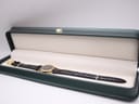 The Raymond Weil watch resting inside a dark green presentation box with a cream interior, laid out flat to display its full length.