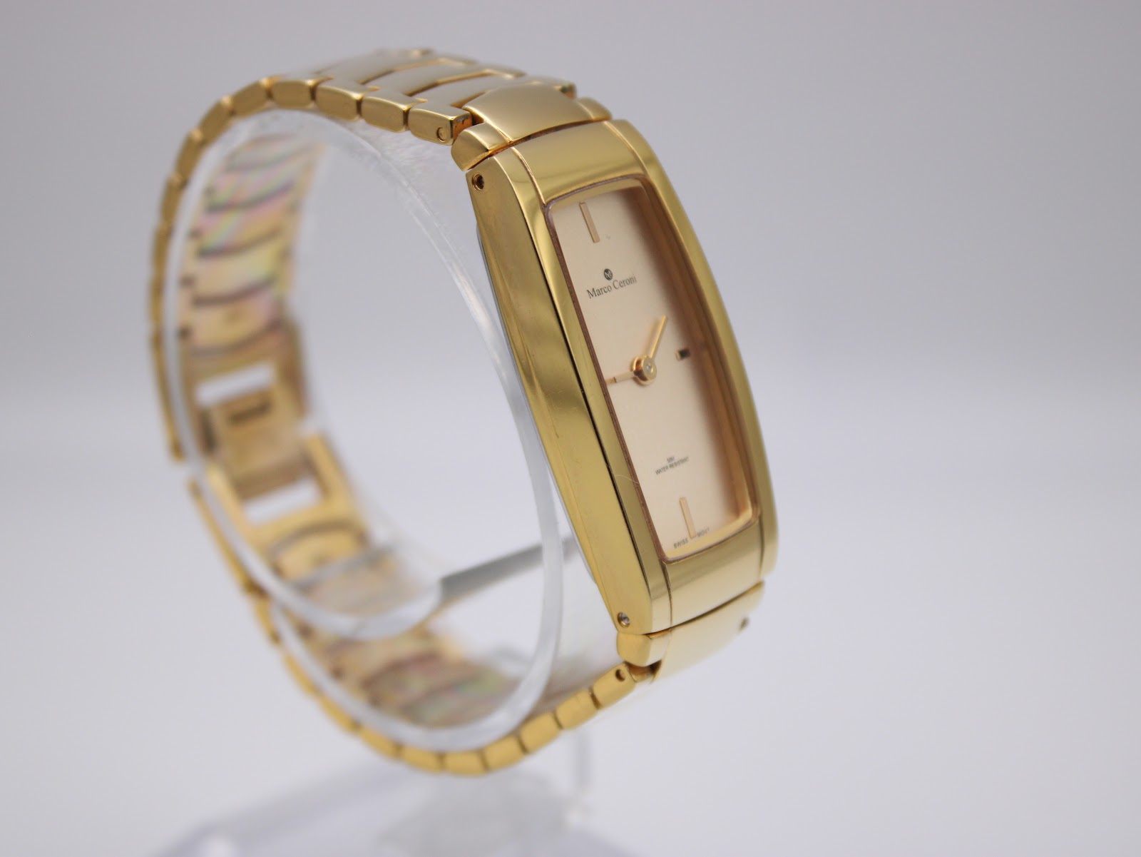 Angled right view of the Marco Ceroni watch on a clear display stand, highlighting the gold-tone finish and slim profile.