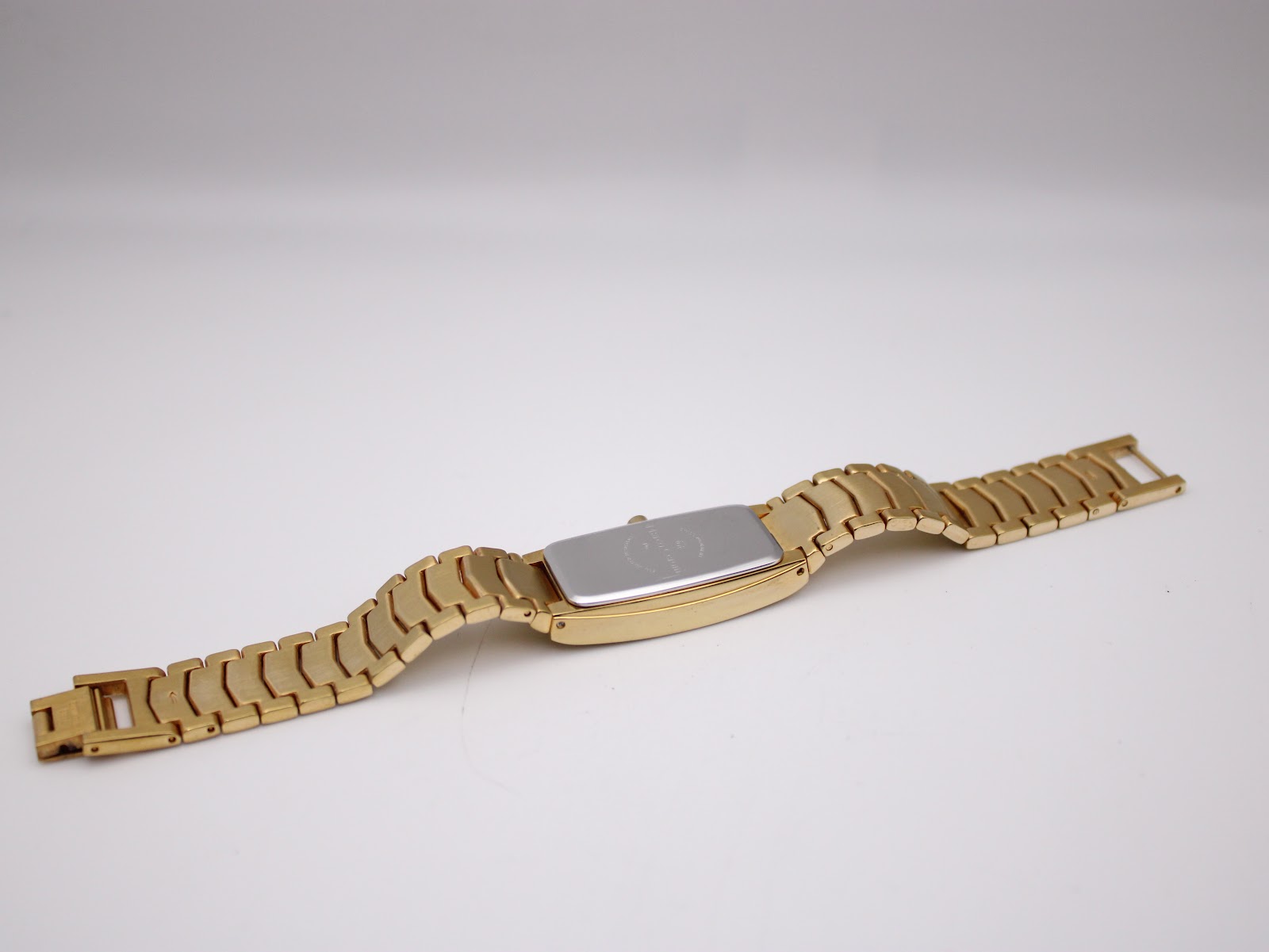 Angled rear view of the extended watch, highlighting the stainless steel case back and the full length of the gold-tone bracelet.
