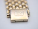 Macro shot of the watch's two-tone integrated bracelet clasp, featuring the engraved 'RW' Raymond Weil logo.