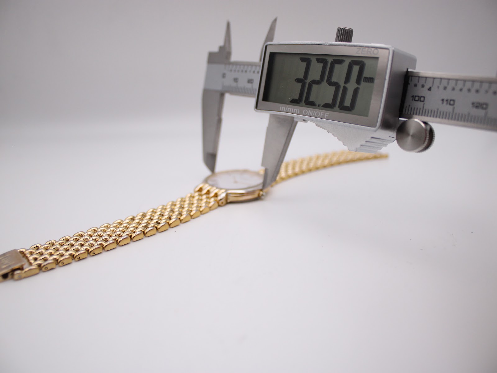 A digital caliper displaying 32.50mm, measuring the case diameter of the Raymond Weil watch.