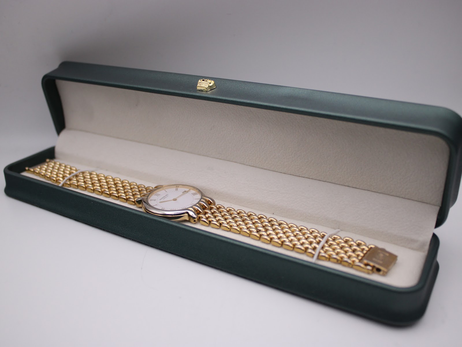 The Raymond Weil watch with its integrated two-tone bracelet resting inside a green watch presentation box.
