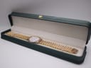 The Raymond Weil watch with its integrated two-tone bracelet resting inside a green watch presentation box.