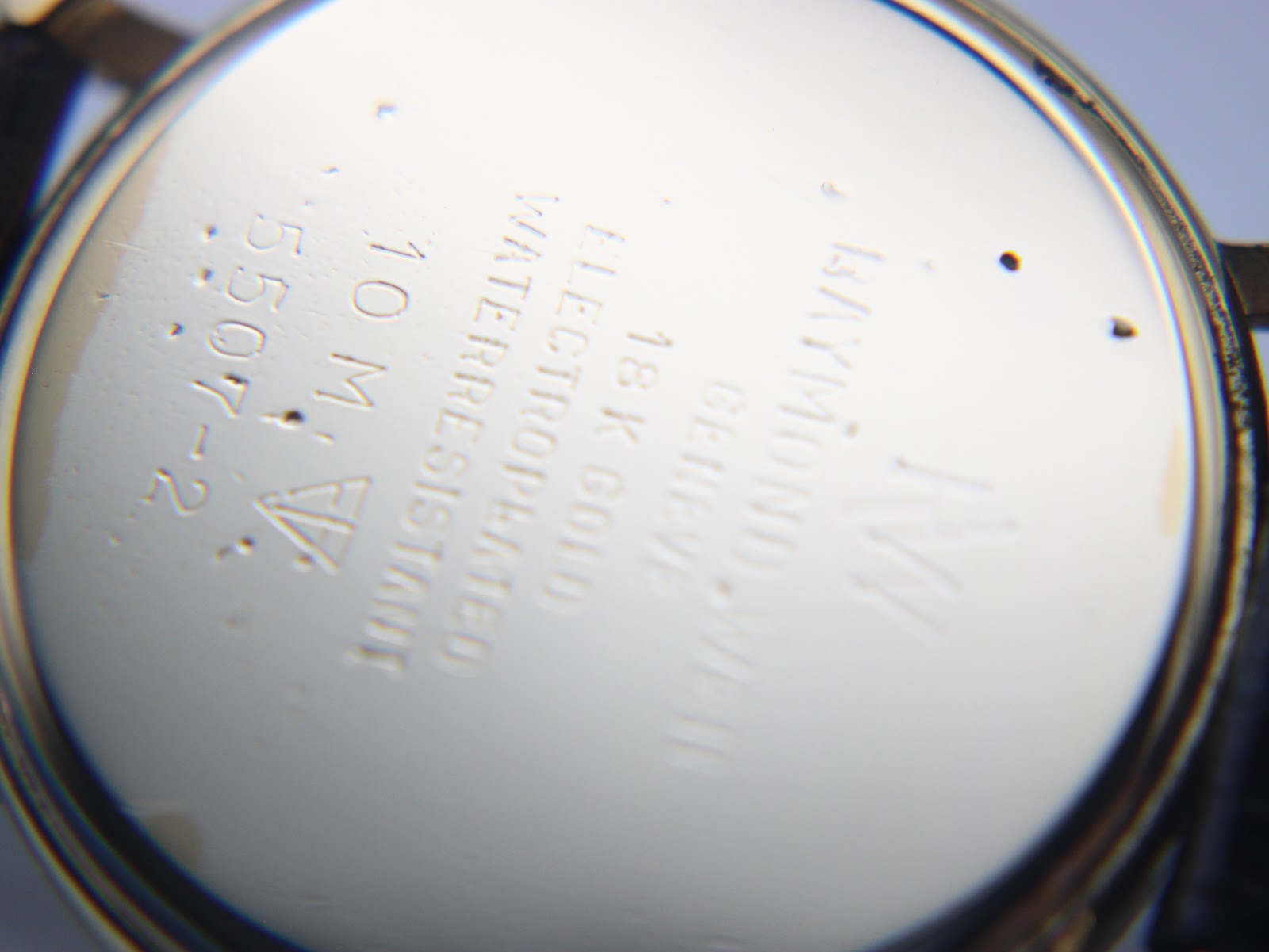 Close-up of the watch case back, showing "Raymond Weil Geneve 18K Gold Electroplated 10 M Water Resistant 5507-2" engravings.