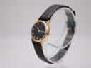 Angled view of the Raymond Weil Geneve watch, showing the gold case, black dial with diamonds, and the texture of the dark brown leather strap.