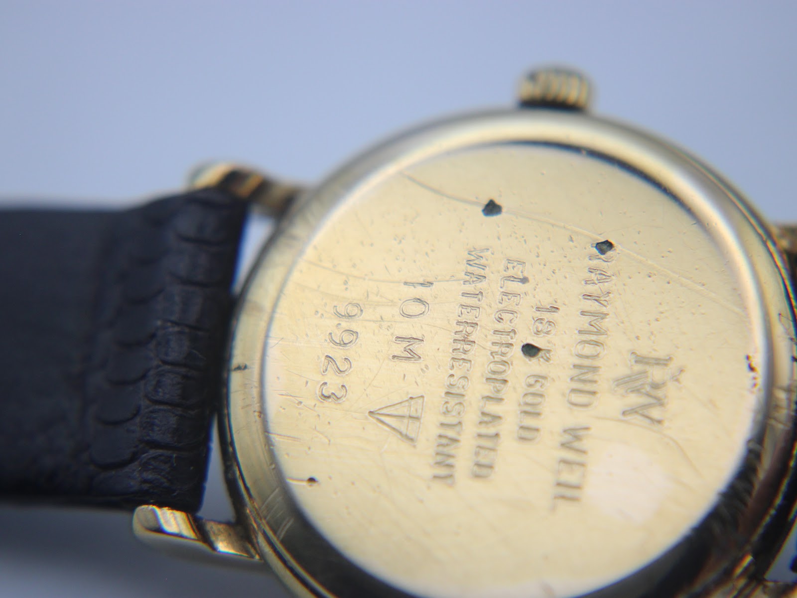 Close-up of the watch case back, revealing engravings: 'RAYMOND WEIL GENEVE', '18K GOLD ELECTROPLATED', 'WATER RESISTANT 10 M', and '9923'.