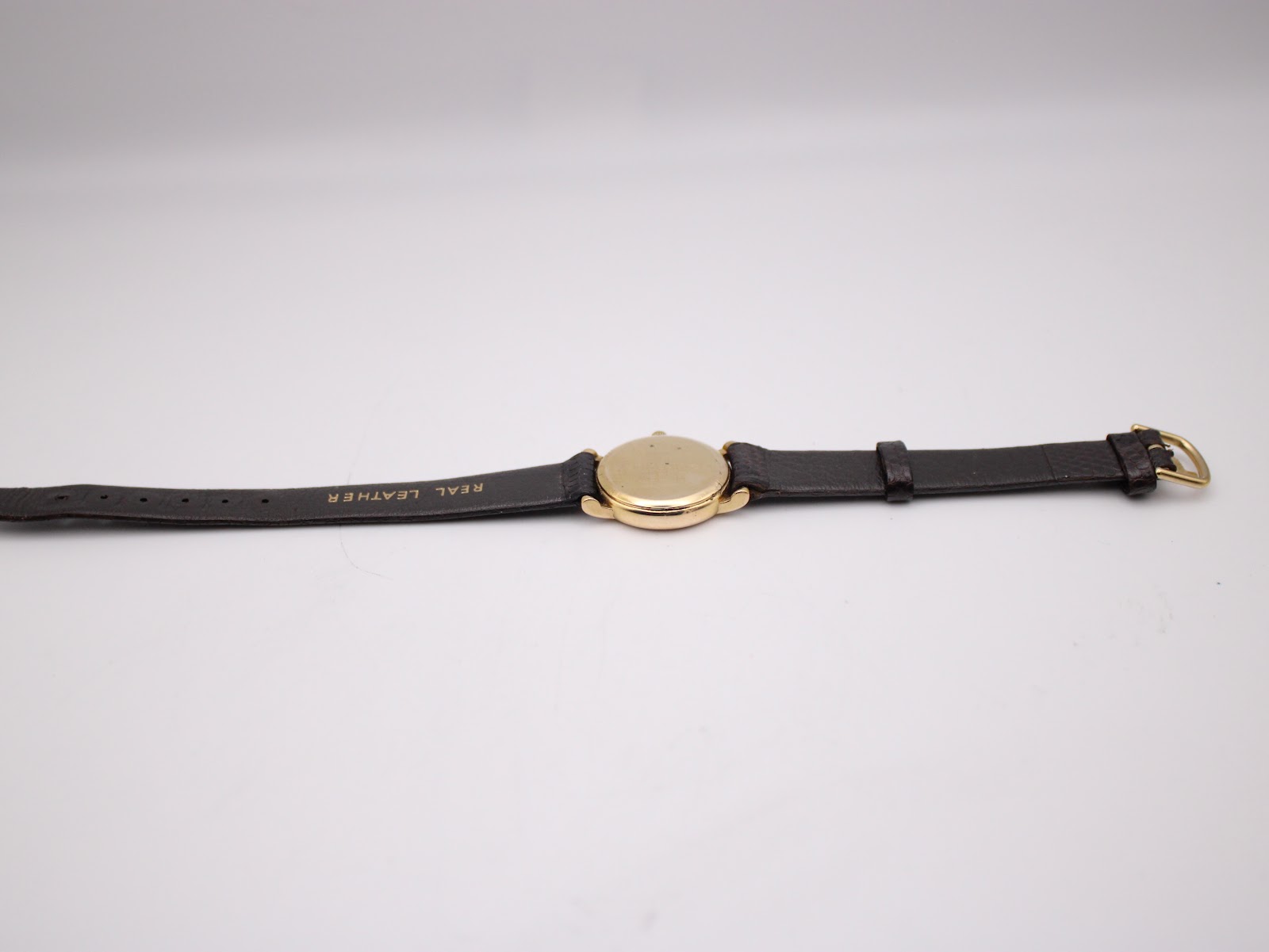 Rear side view of the Raymond Weil watch and strap laid flat, showing the 'REAL LEATHER' embossing on the strap interior and the gold-tone buckle.