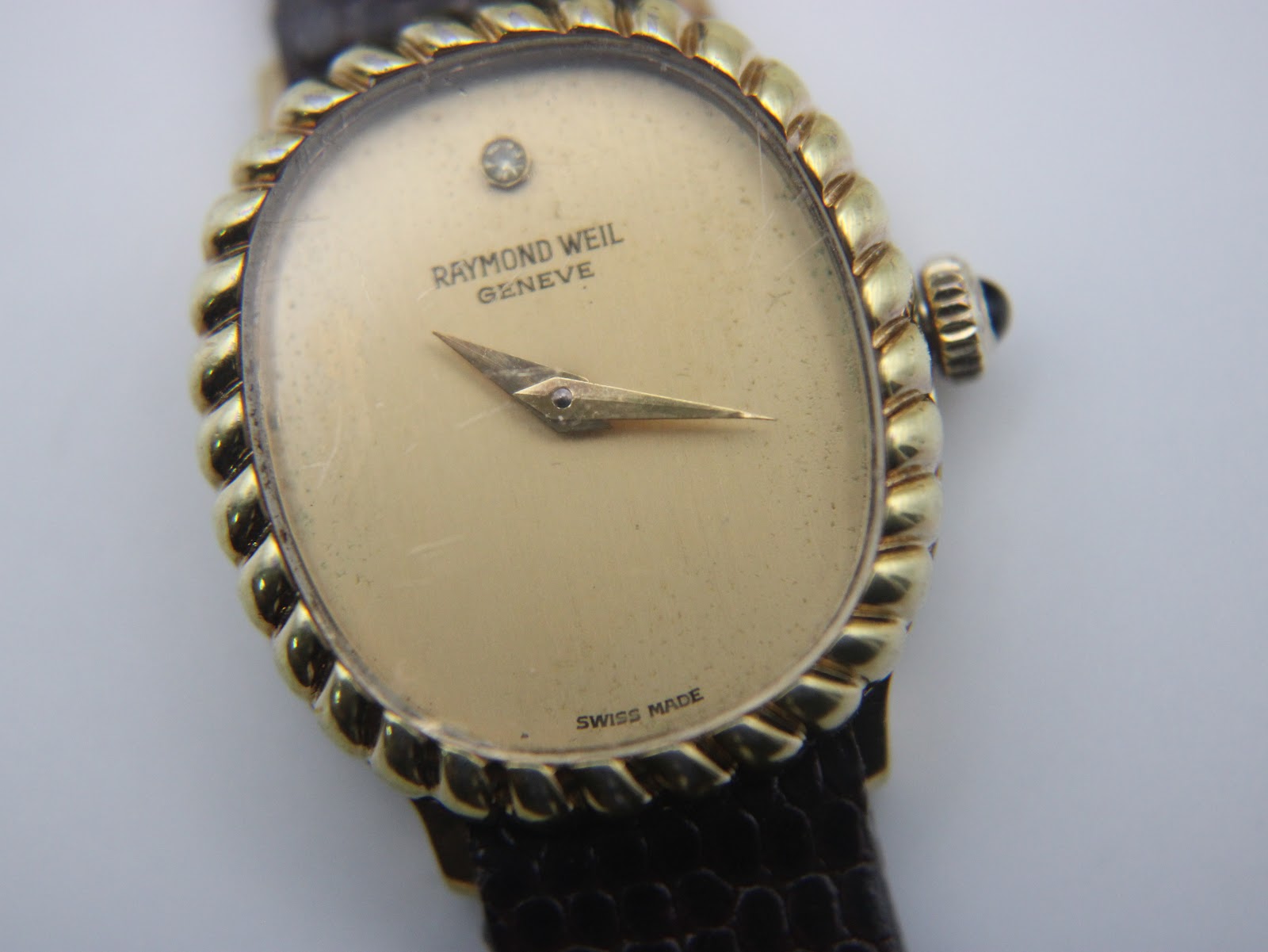 Close-up of the champagne dial, showing Raymond Weil logo, single diamond marker, gold hands, and subtle crystal scratches.