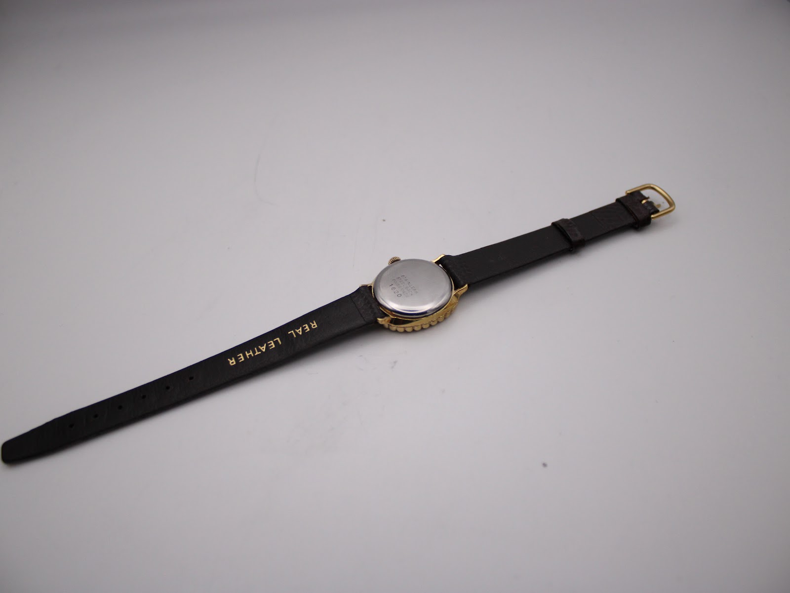 Back view of the watch and strap, showing the stainless steel case back and 'REAL LEATHER' stamped on the strap.