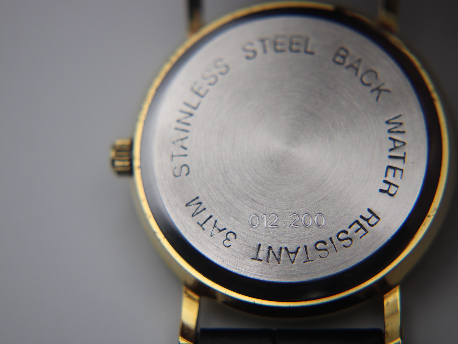 Close-up of the brushed stainless steel case back, engraved with 'STAINLESS STEEL BACK WATER RESISTANT 3ATM 012.200'.