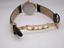 Close-up of the gold-tone deployant clasp, open and unfurled on the black leather strap.