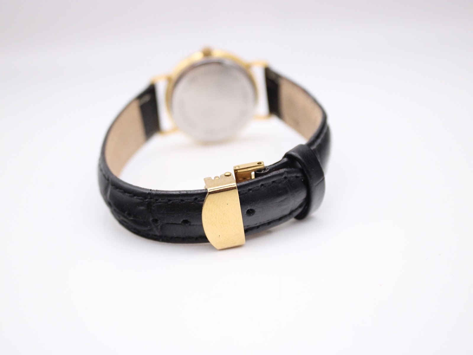 Close-up of the gold-tone deployant clasp, closed on the black leather strap, showing its sleek design.