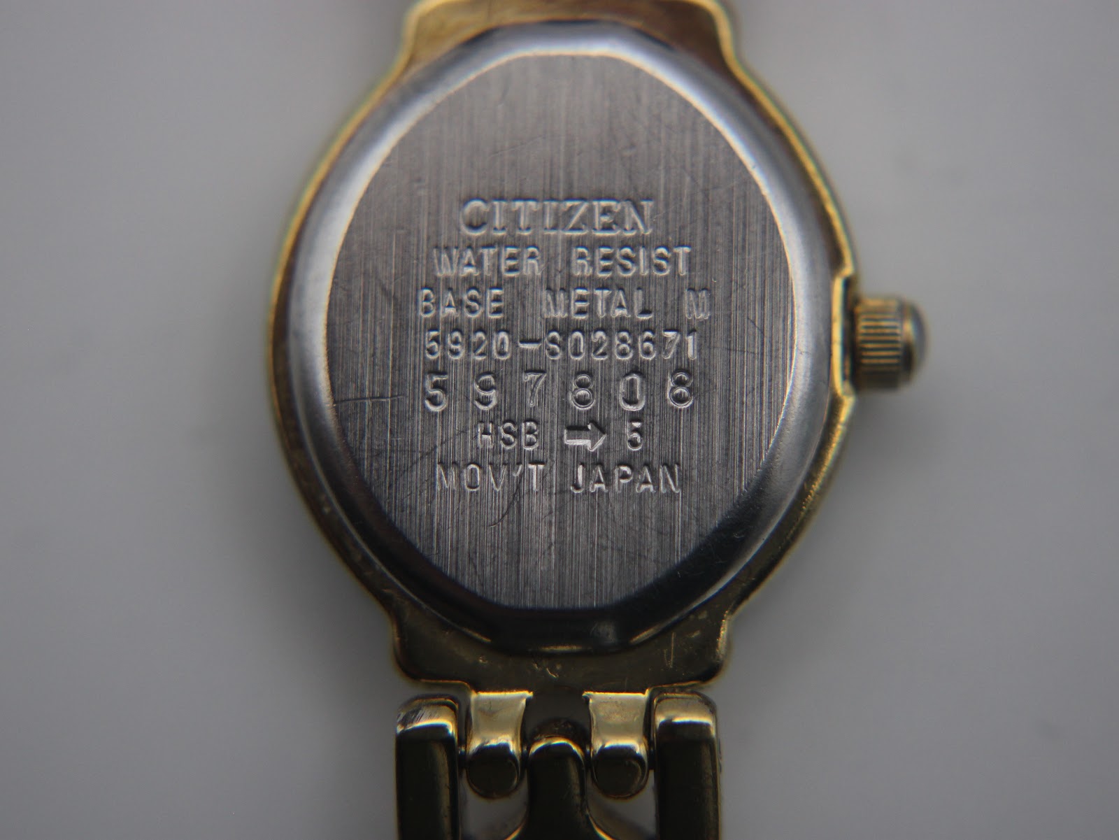 Close-up of the watch case back, showing 'CITIZEN', 'WATER RESIST', 'BASE METAL', '5920-S023871', serial number '597808', and 'MOV'T JAPAN' engravings.