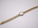 Overhead view of the full watch and integrated gold-tone steel bracelet laid flat, front side up.