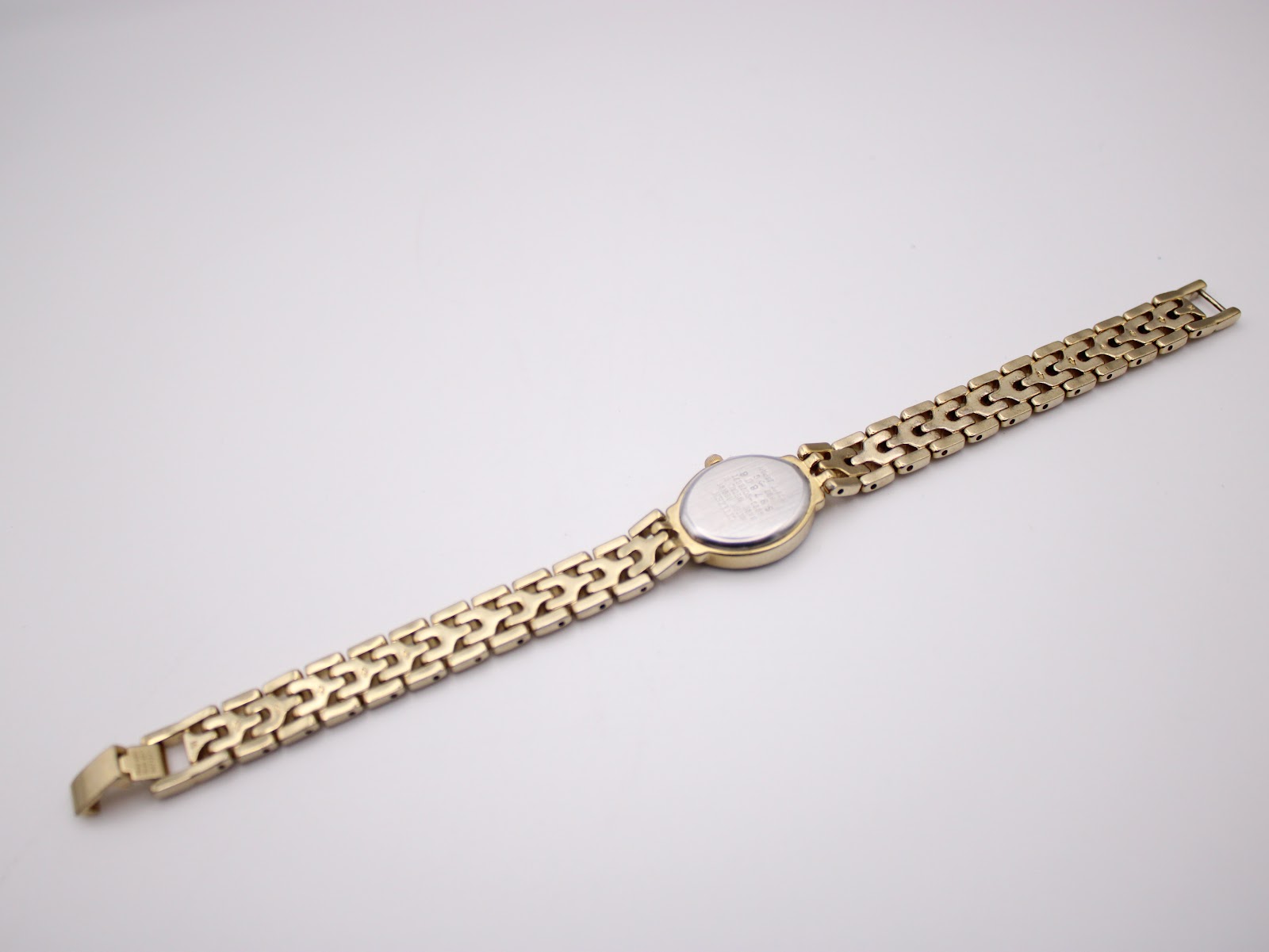 Rear view of the full watch and integrated gold-tone steel bracelet laid flat, showing the case back and bracelet underside.