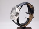 Right-side profile view of the Avon watch showing the silver-tone case, crown, and navy blue leather strap on a watch stand.
