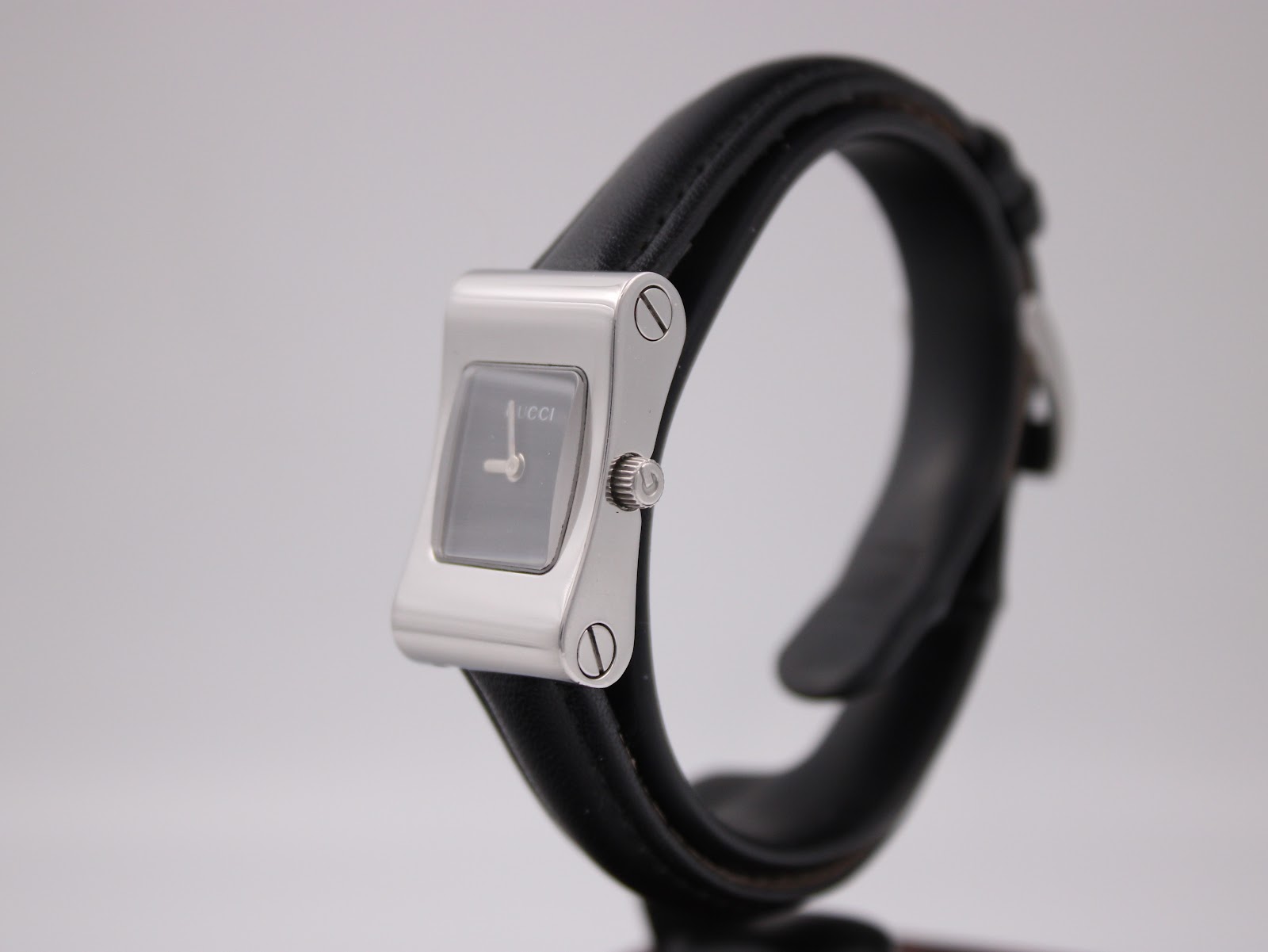 Angled view of the Gucci 2300L showing the right side of the silver rectangular case, crown, and black leather strap.