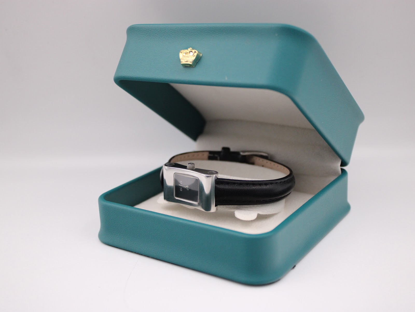 The Gucci 2300L watch resting inside a teal presentation box with a gold crown emblem.
