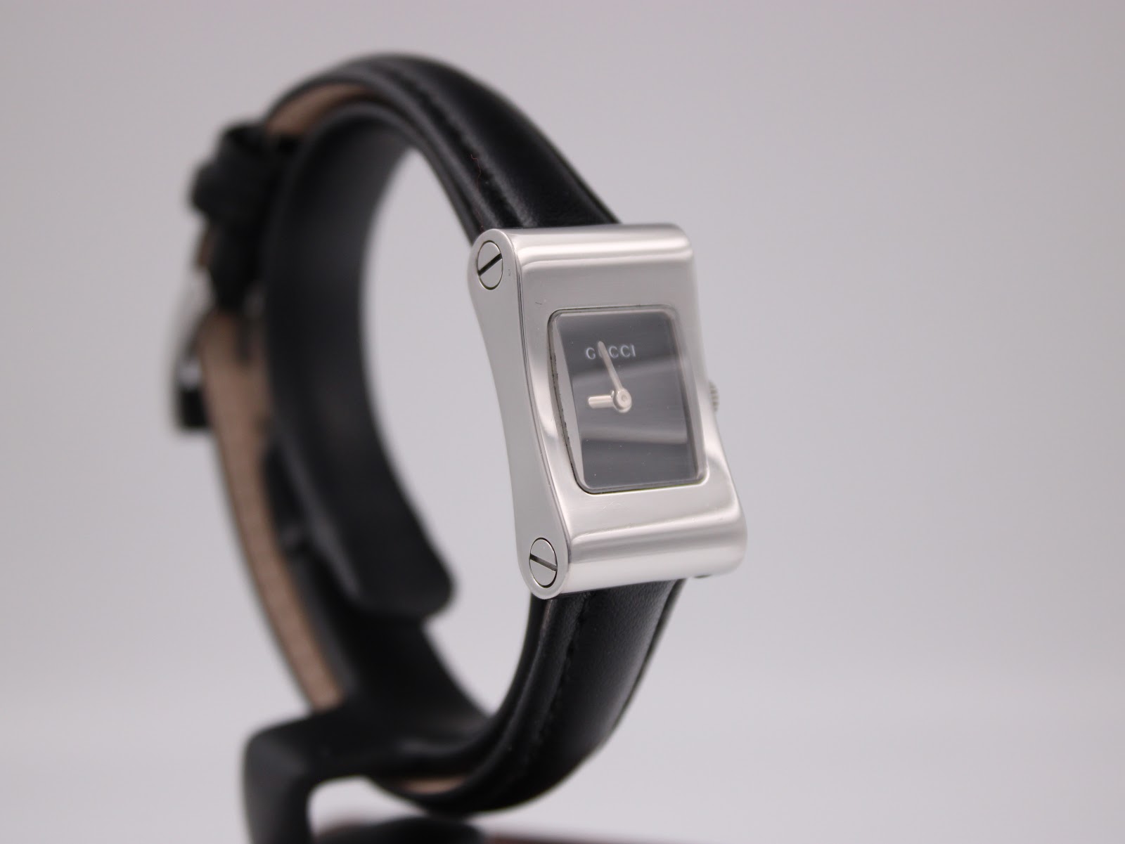 Angled view of the Gucci 2300L showing the left side of the silver rectangular case and black leather strap.