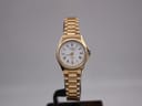 Front view of gold plated Rotary watch with white dial and Roman numerals on a dark stand, set against a grey background.