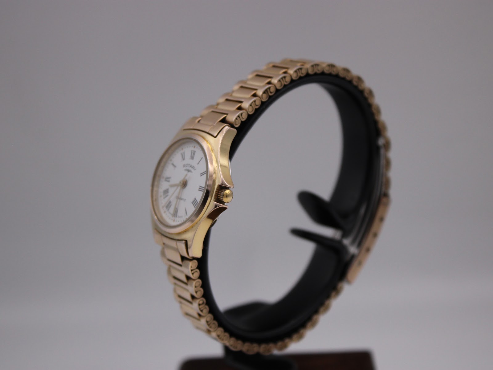Side-angle view of the gold plated Rotary watch on a black display stand, showing the crown and case profile.
