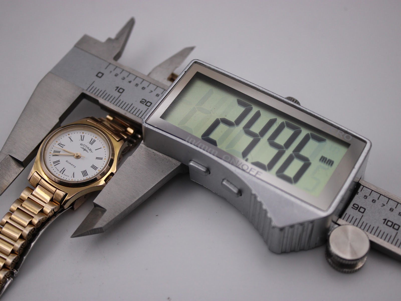 Digital caliper measuring the watch case diameter, displaying an exact measurement of 24.96 mm.
