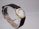 Oblique front-left view of the Tissot Stylist on a clear stand, highlighting the gold case and strap texture