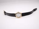Full view of the Tissot Stylist watch laid flat, displaying the gold case and black leather strap with buckle