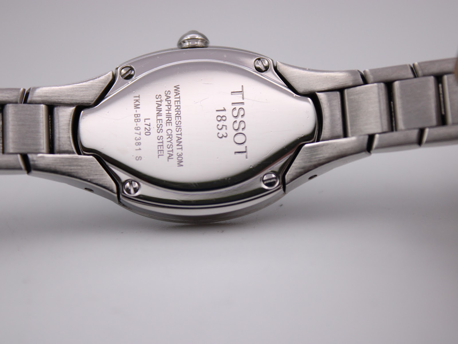 Close-up of the watch case back, engraved with "TISSOT 1853", "WATERRESISTANT 30M", "SAPPHIRE CRYSTAL", "STAINLESS STEEL", "L720", and serial number "TKM-BB-97381 S".