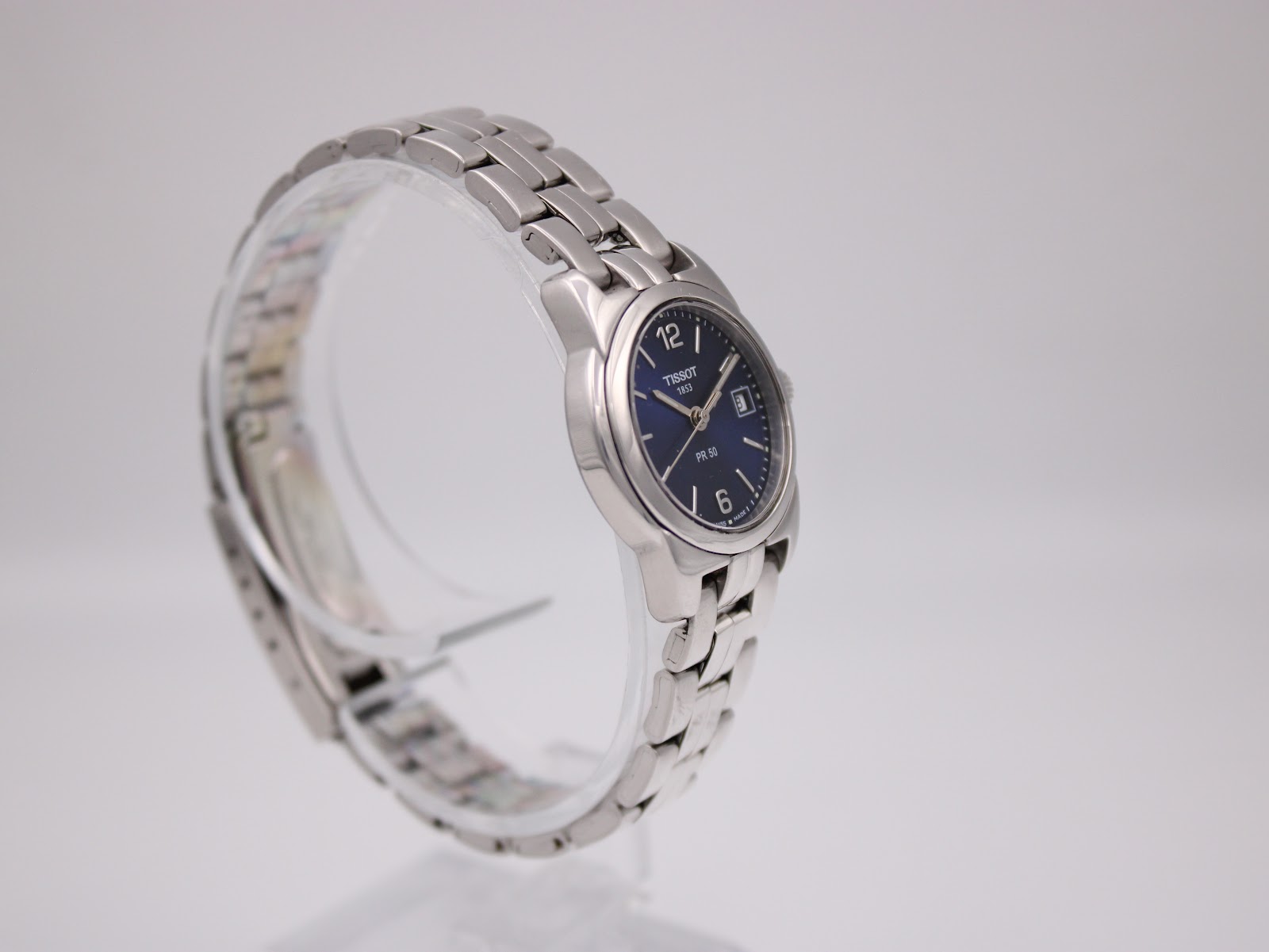 Three-quarter view of the Tissot PR 50 watch on a stand, showing the signed crown and bracelet.