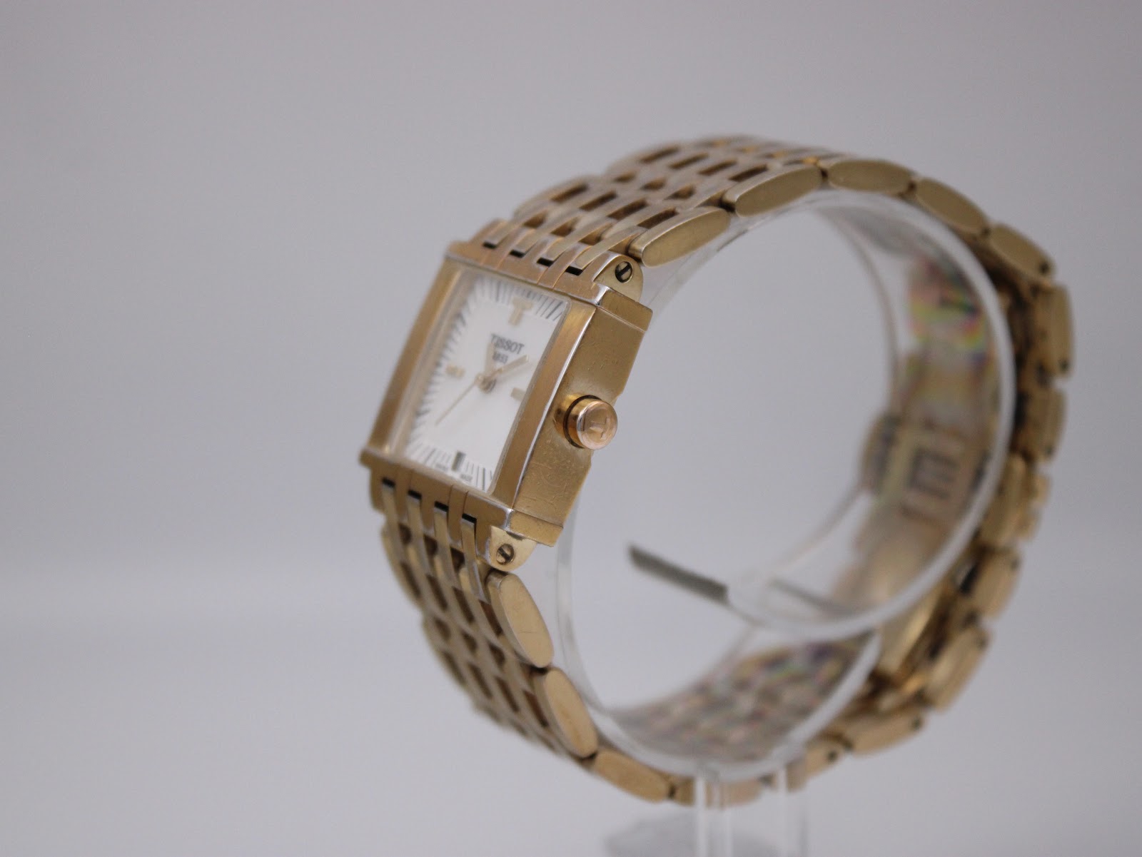 Side view of the Tissot L910 watch on a clear stand, showing the integrated gold-tone bracelet.