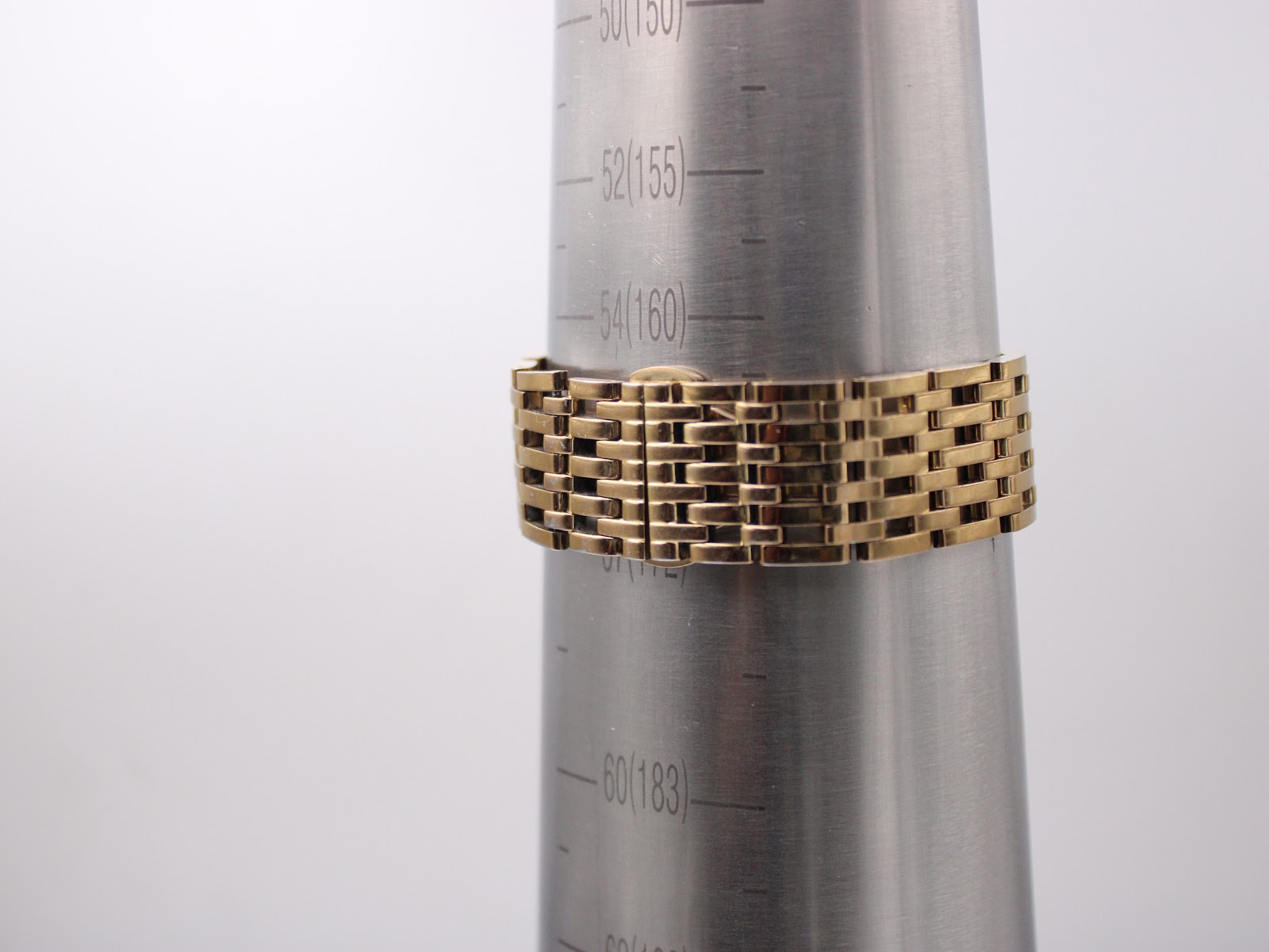 Gold-tone brick-link bracelet of the Tissot watch wrapped around a wrist sizing cone, showing wrist size markings.
