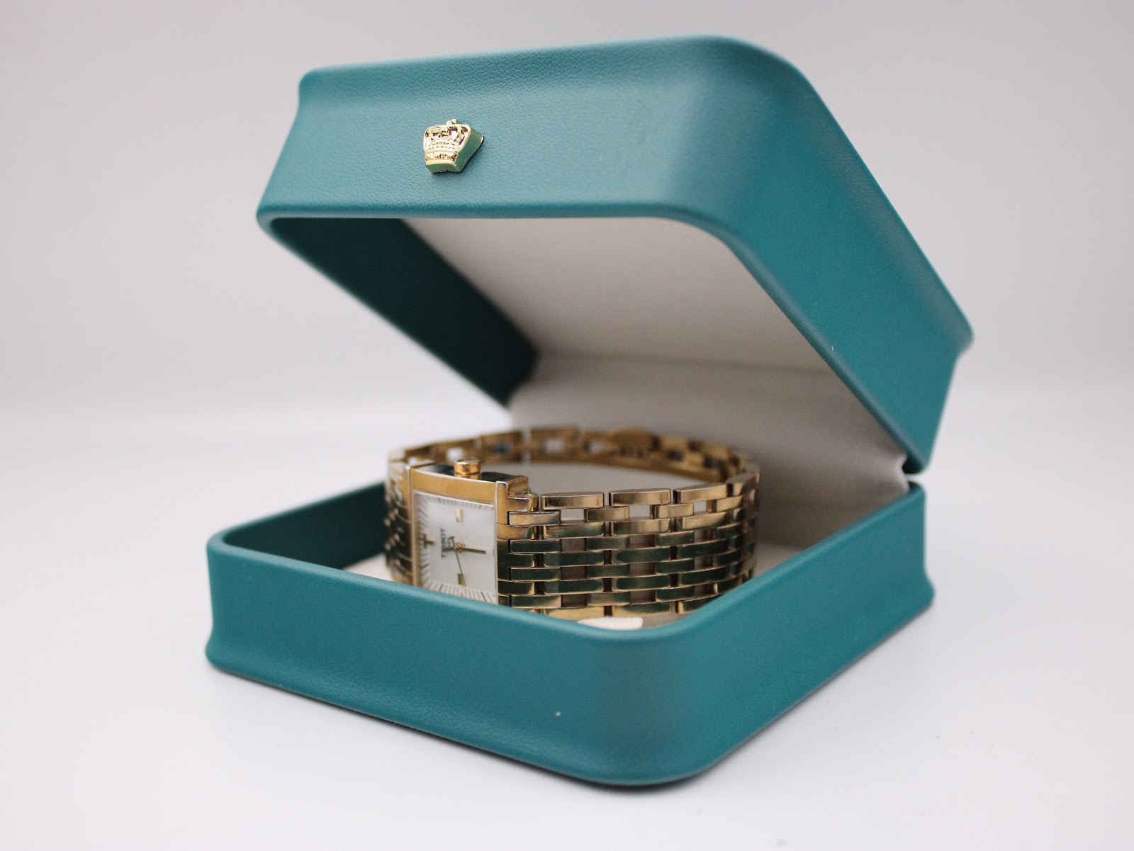 Tissot L910 gold-tone watch nestled in an open, teal-coloured watch box.
