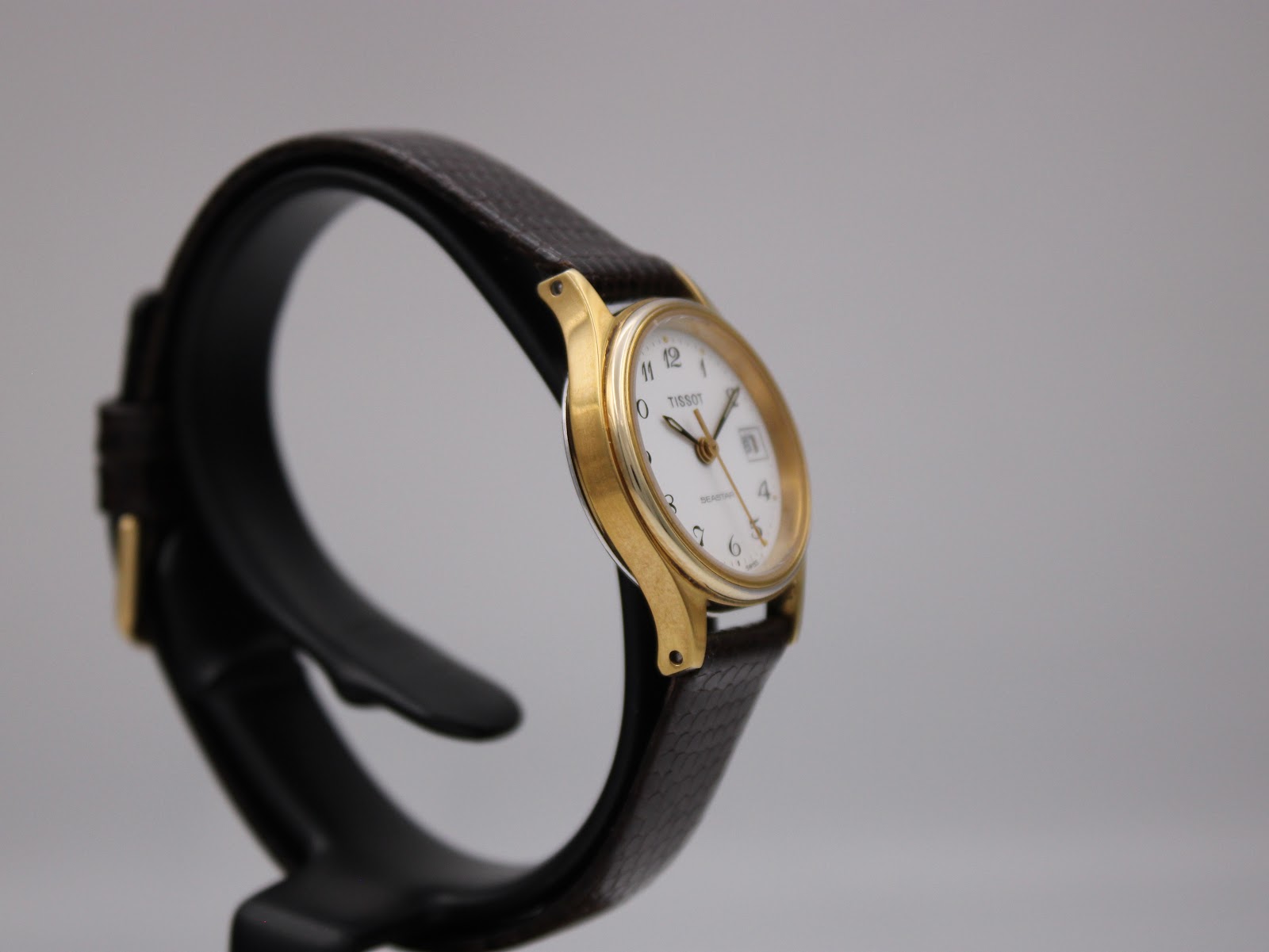 Left side view of the Tissot Seastar on a watch stand, highlighting the gold-plated case.