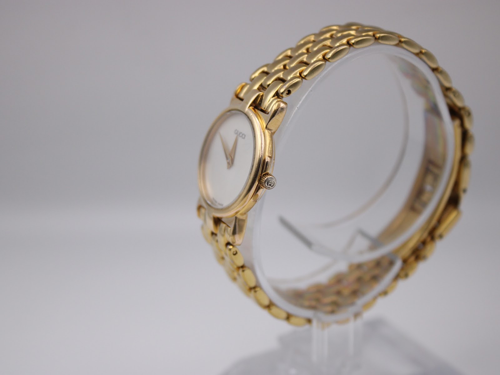 Angled side view of the Gucci 3400L watch on a clear display stand, showing the case profile and signed crown.