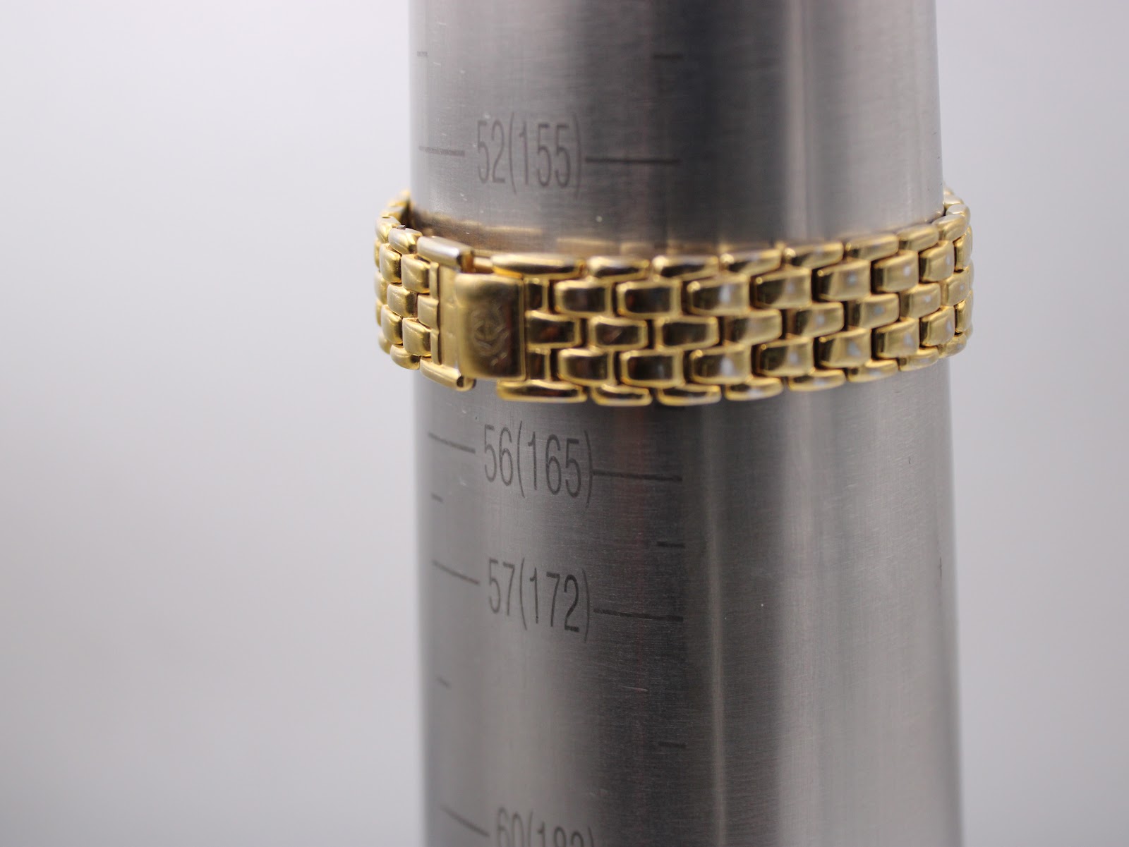 The gold plated multi-link bracelet of the Gucci watch wrapped around a metal wrist sizing gauge, indicating it fits a wrist of approximately 16cm.
