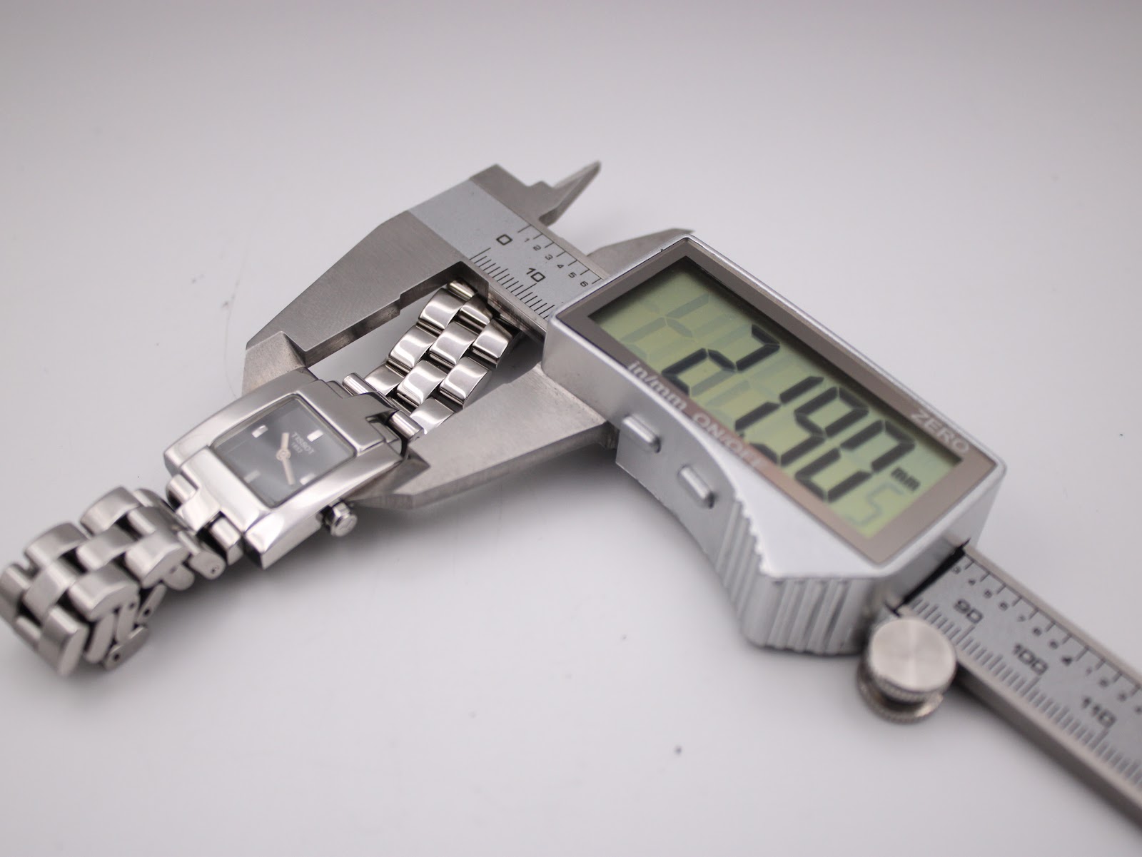 The Tissot watch case being measured by a digital caliper, displaying a precise width of 21.90mm.
