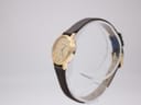 Angled side view of the gold-plated Tissot watch on a clear stand, showing the case profile.