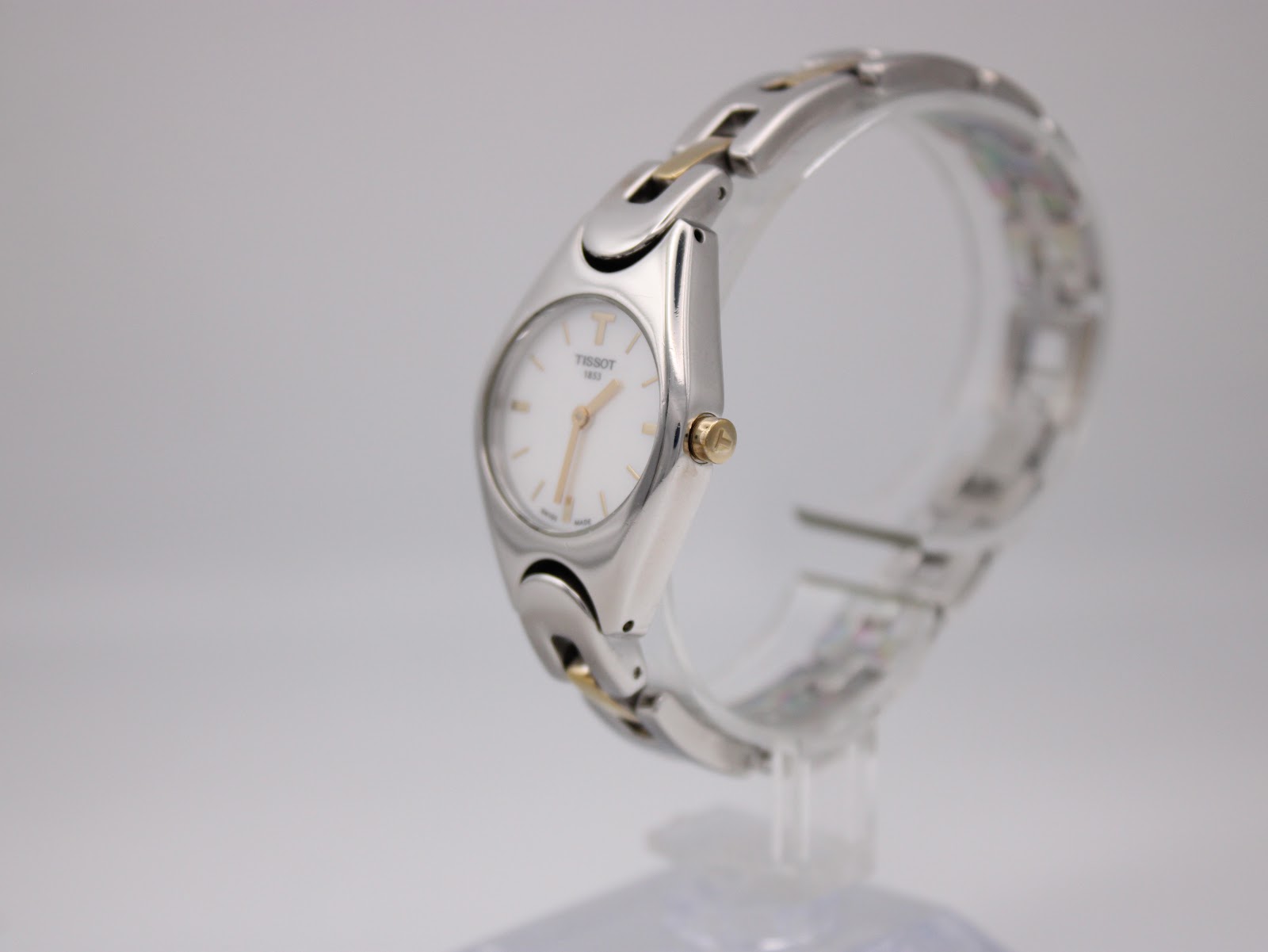 Side profile view of the Tissot T-Trend watch on a stand, highlighting the gold-tone crown and integrated bracelet design.