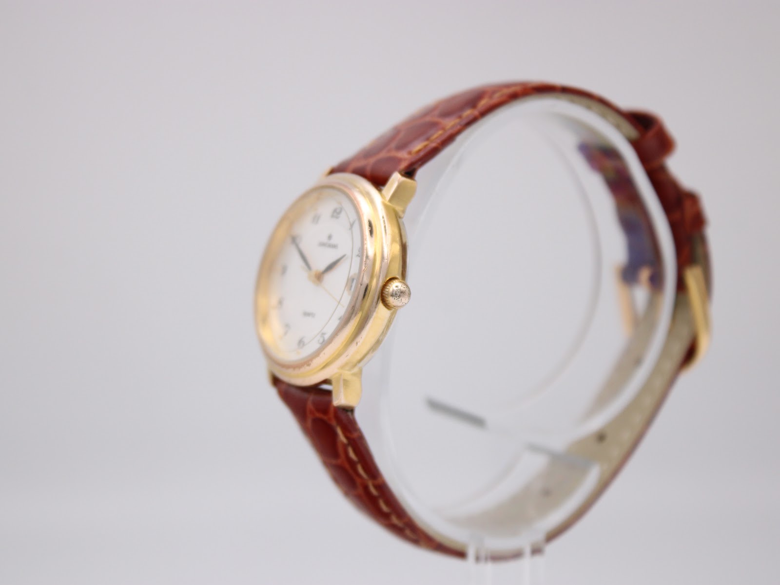 Side view of the Junghans watch on a clear stand, showing the gold-tone case and crown.