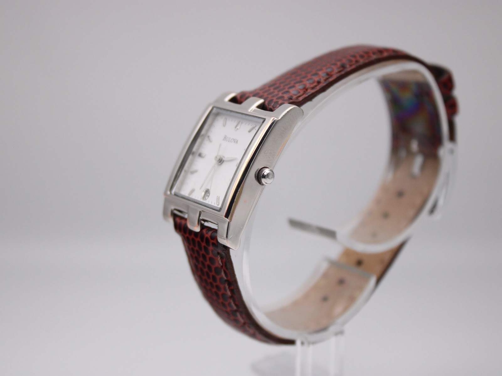 Angled side view of the Bulova watch on a clear display stand, showing the case profile and strap texture.