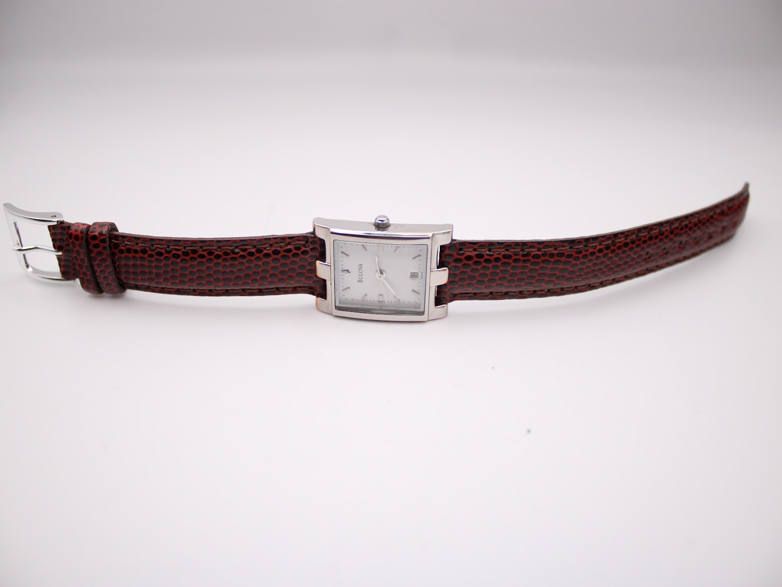 Overhead view of the Bulova watch with its burgundy lizard-grain leather strap extended flat.