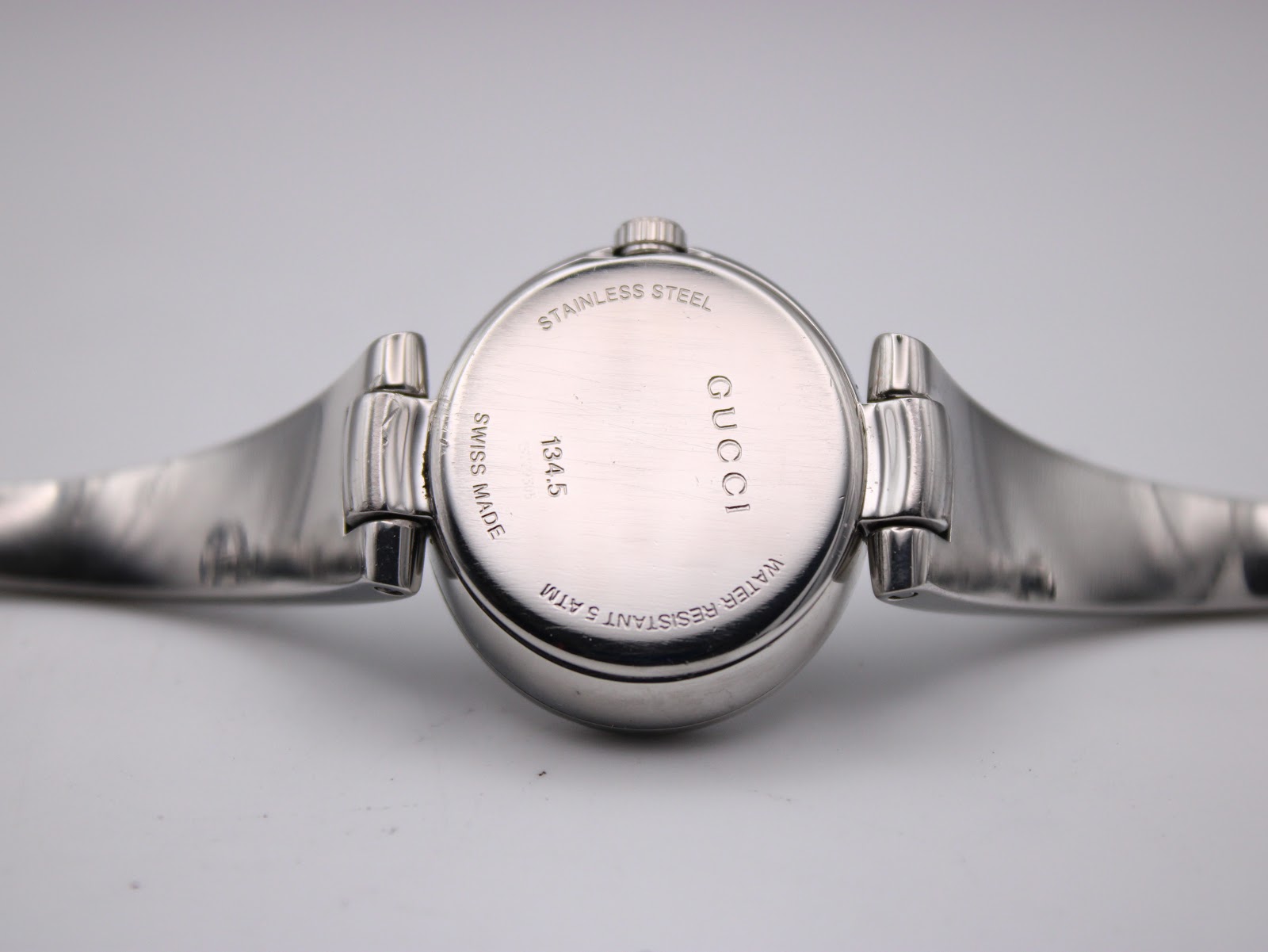 Close-up of the watch case back showing 'STAINLESS STEEL', 'GUCCI', '134.5', 'WATER RESISTANT 5 ATM', and 'SWISS MADE' engravings.