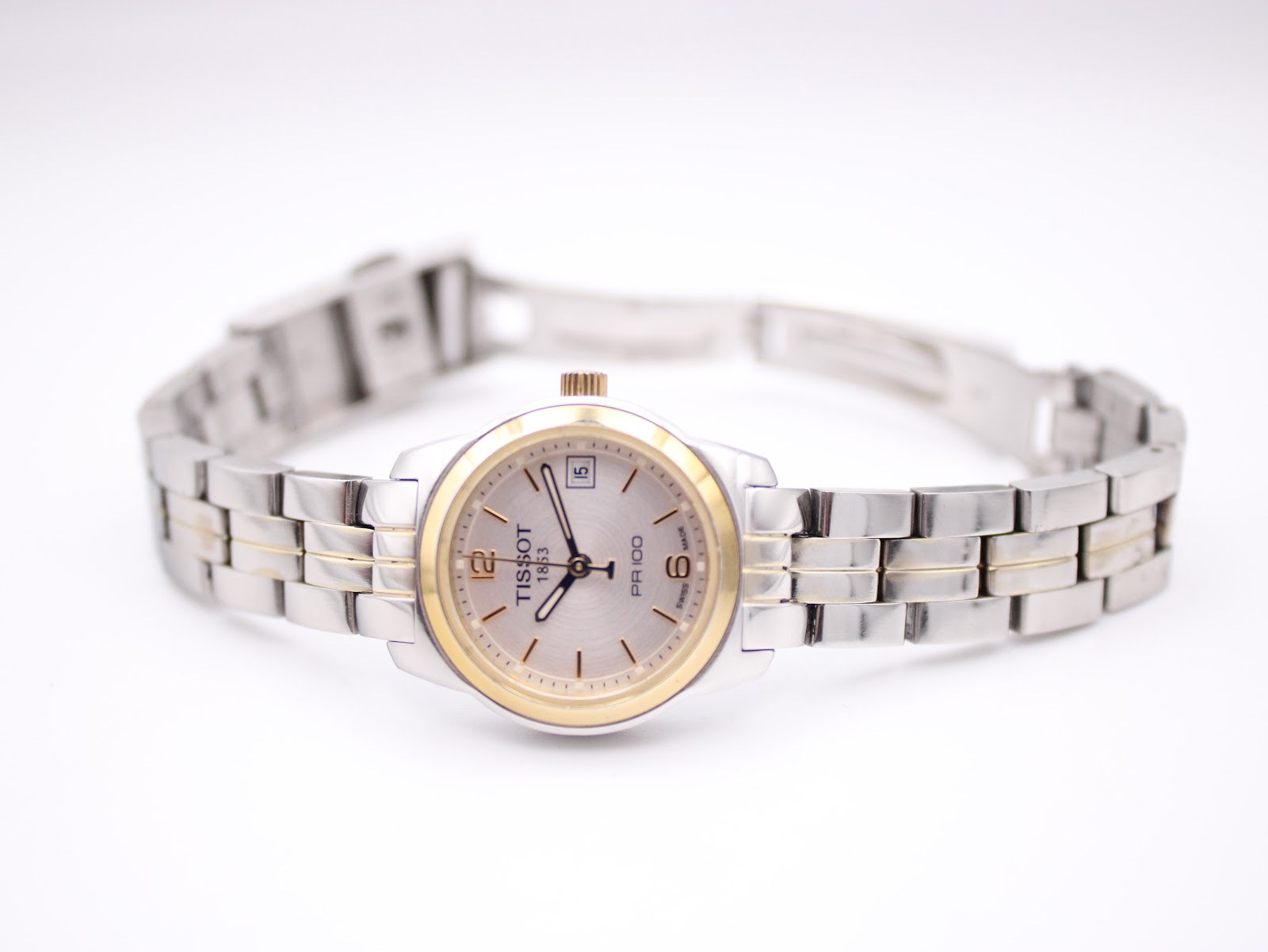 Full front view of the Tissot PR 100 watch with its two-tone bracelet laid flat, showcasing the entire timepiece.
