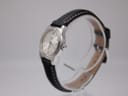 Side view of the Tissot watch on a clear stand, showing the crown and polished stainless steel case.