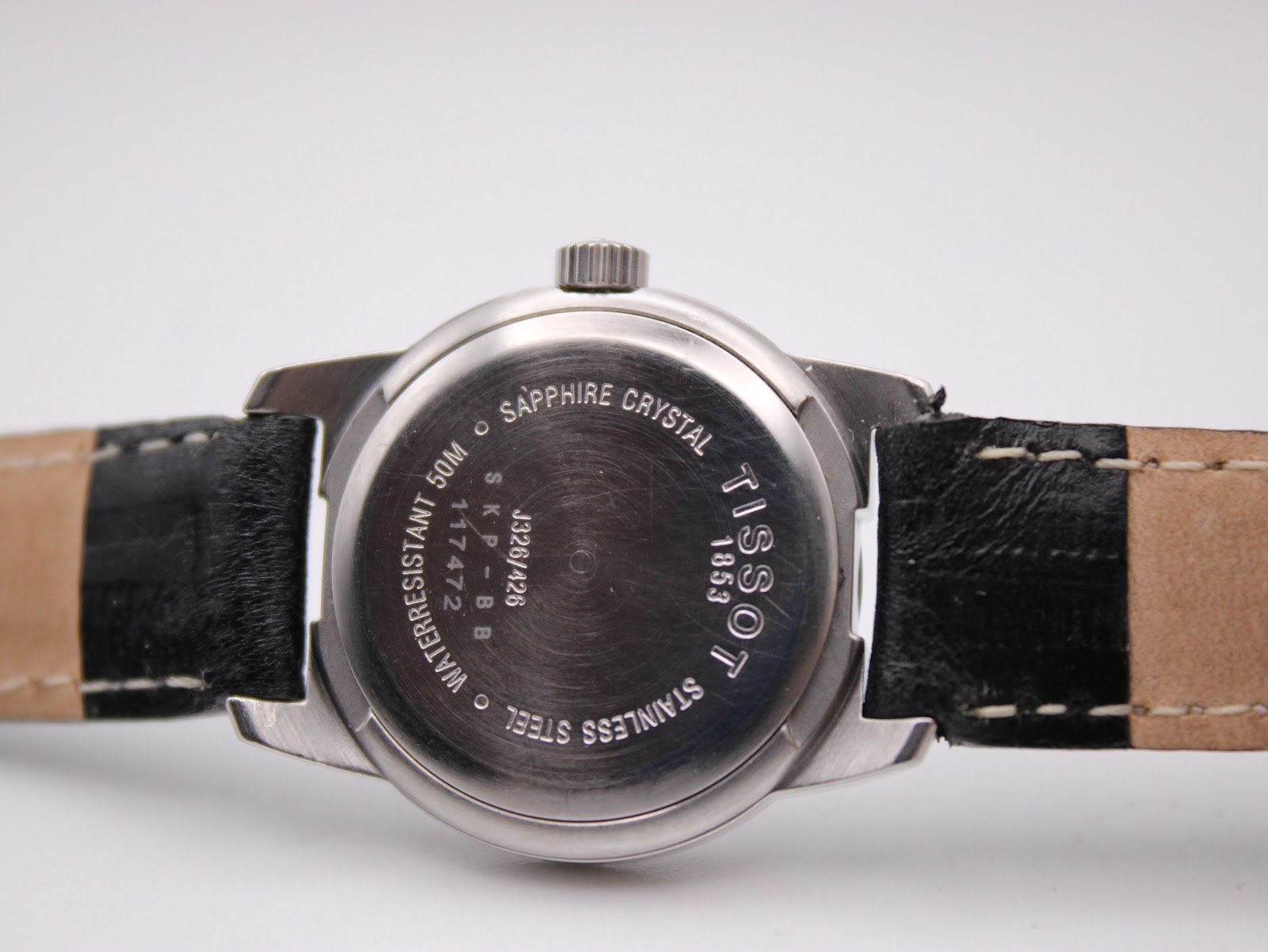 Close-up of the Tissot watch case back, showing 'sapphire crystal', 'waterresistant 50m', 'stainless steel', and model number J326426.
