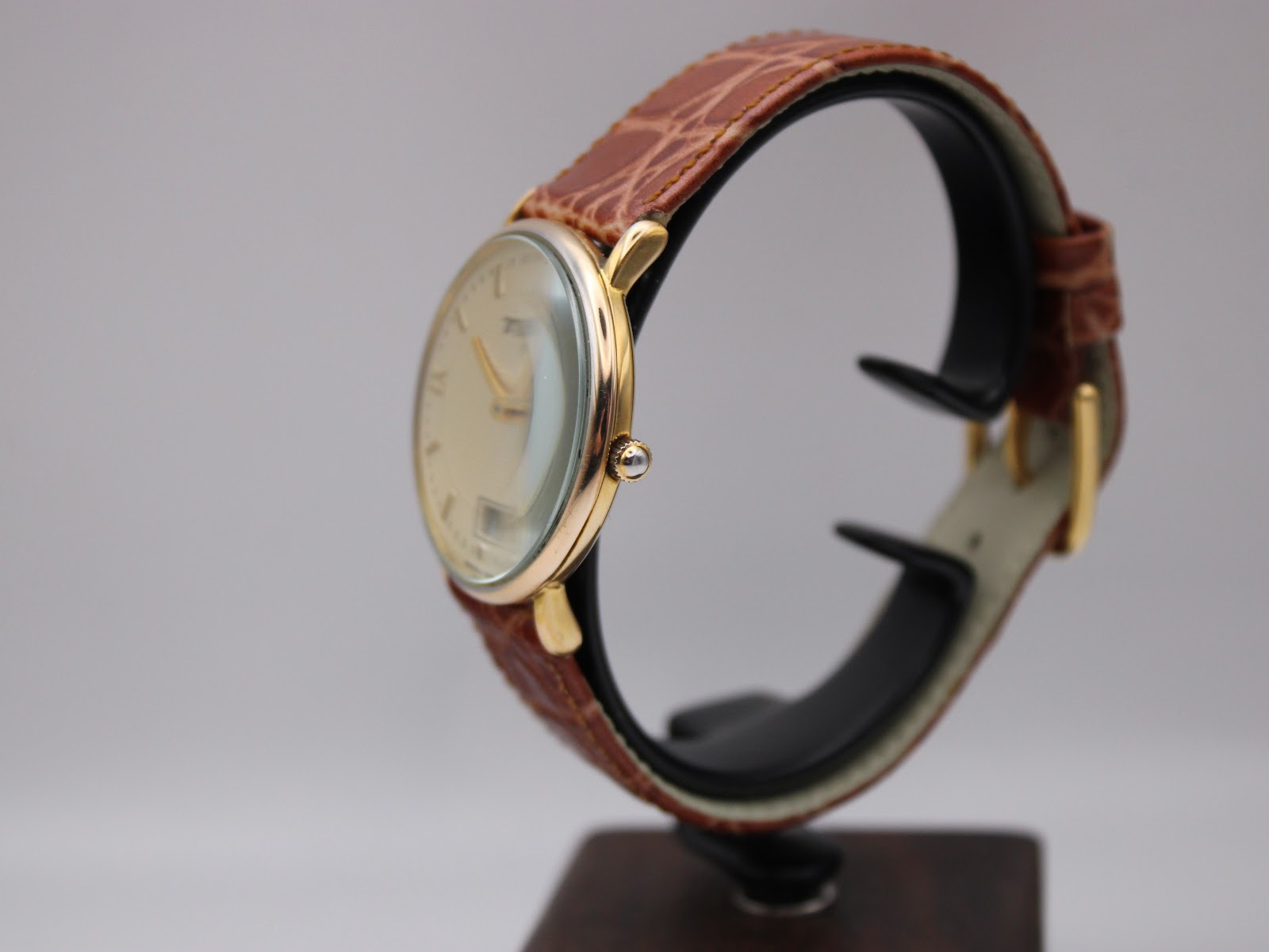 Side view of the Tissot T890K watch on a stand, showing the curved gold plated case and profile of the mineral glass.